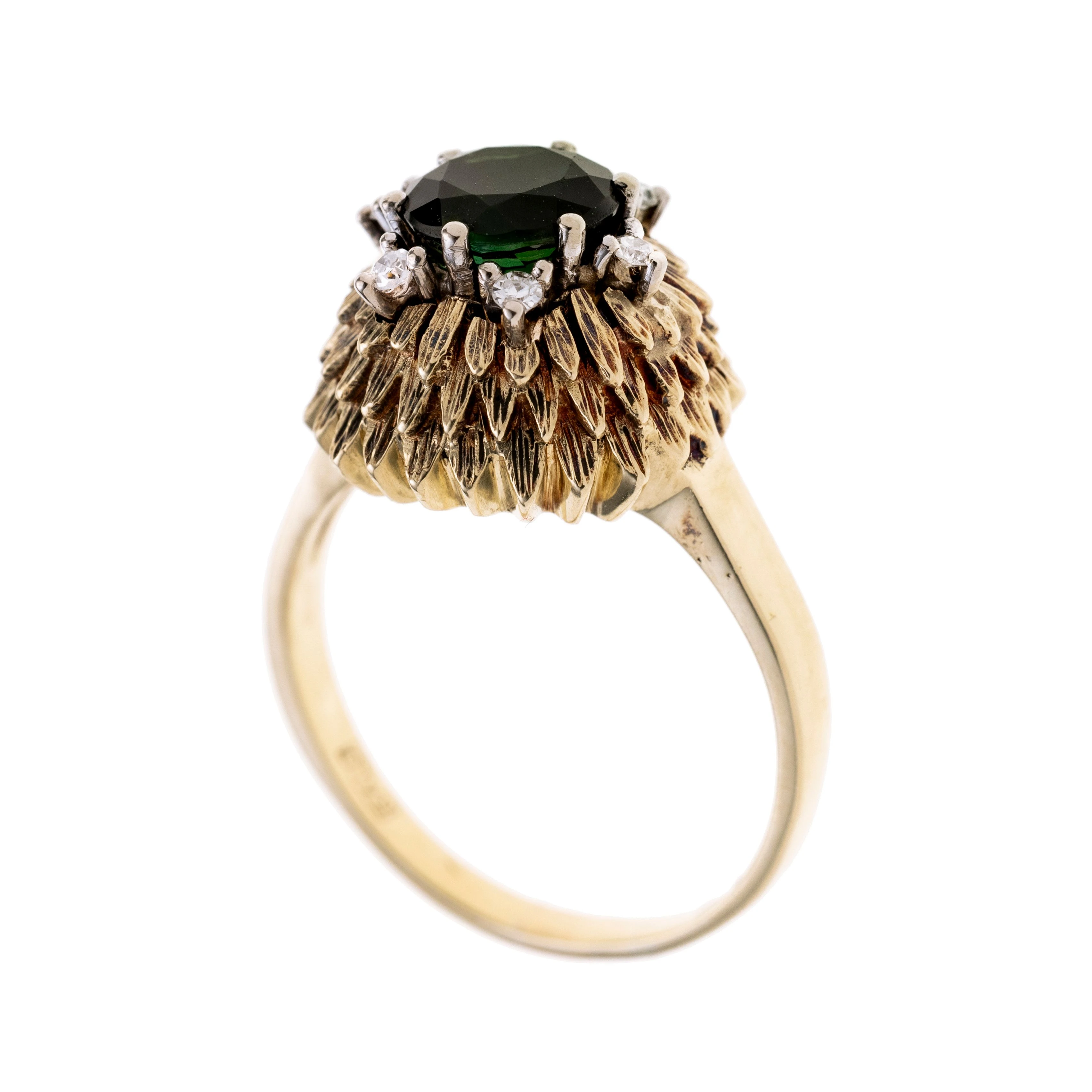 Ein grüner Turmalin mit sechs Brillanten ringsum, alle Steine in Krappen gefasst. Darunter liegend Blätter zur Verzierung.