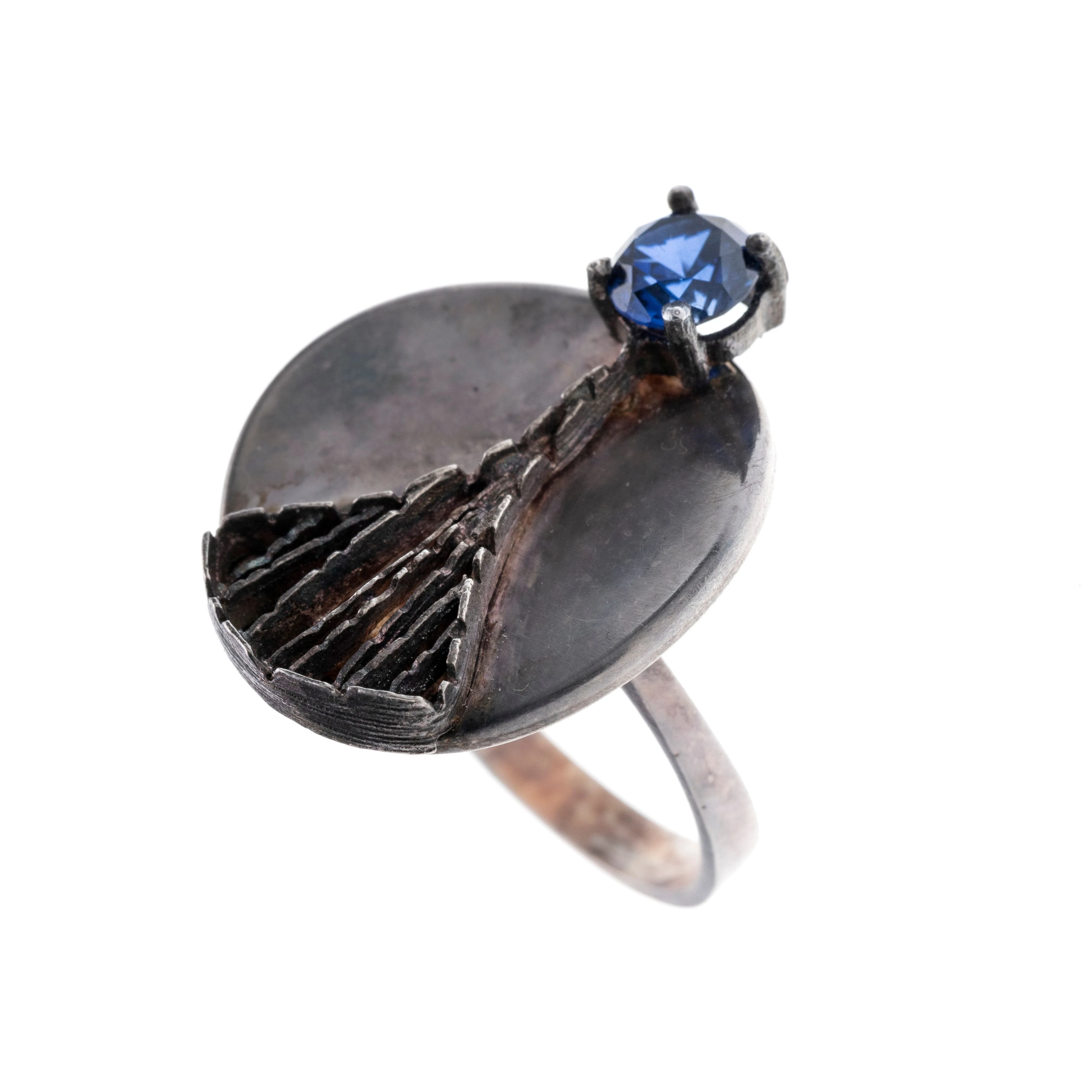 Ein Ring mit rundem Ringkopf, abstrakt zulaufendem Geflecht und einem dunkelblauen Glasstein. Autorenschmuck.