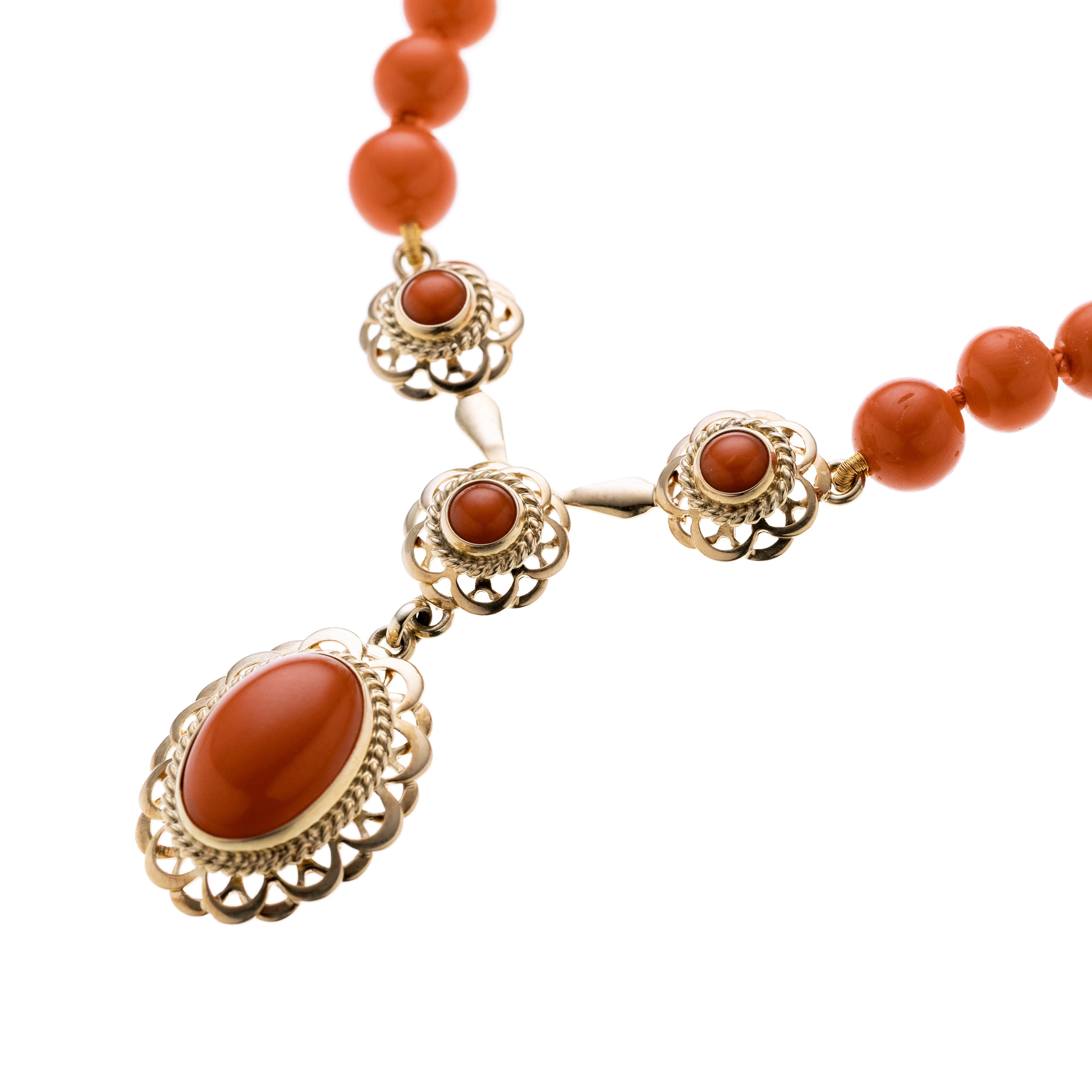 Eine Korallenkette im Verlauf, mittig hängt ein aus gelbgold bestehendes Element mit Bogenelementen verziert und vier Korall-Cabochons dazwischen gesetzt.