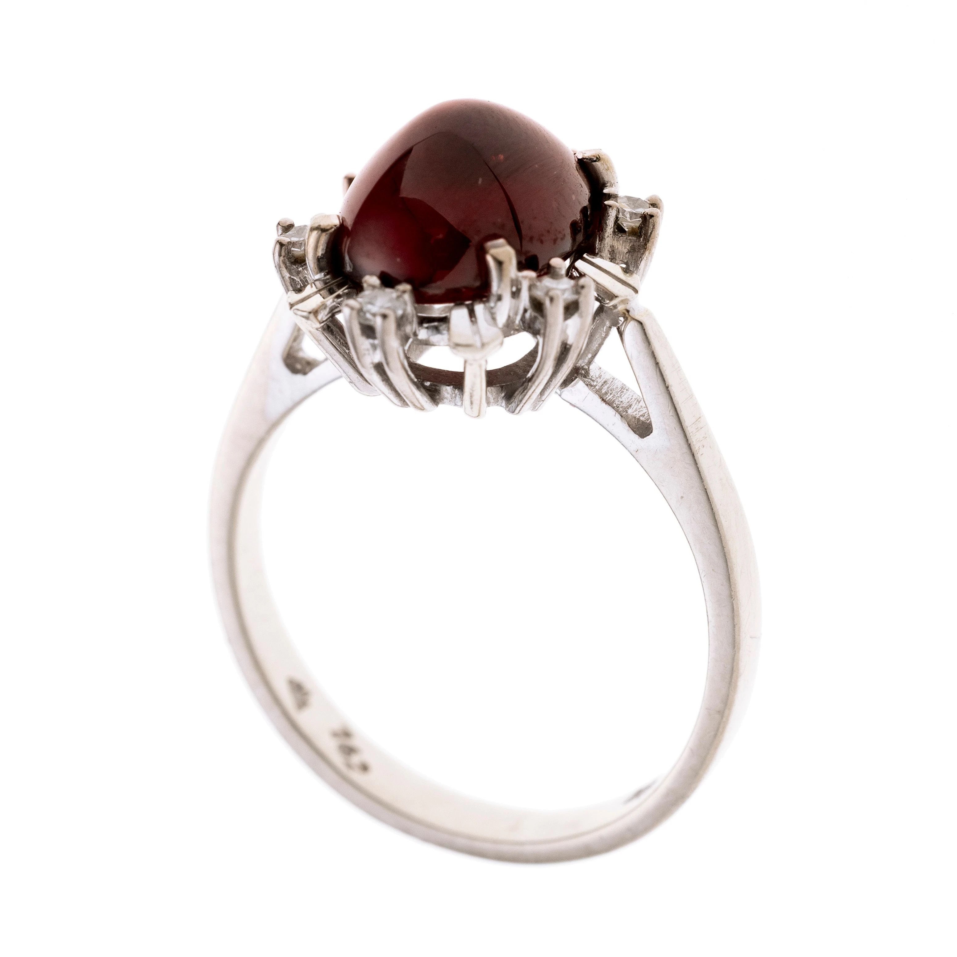 Ein Damenring gefertigt aus Weißgold mit einem ovalen Granat-Cabochon und einem Kranz aus 6 Achtkant-Diamanten von insg. ca. 0,12 ct.
