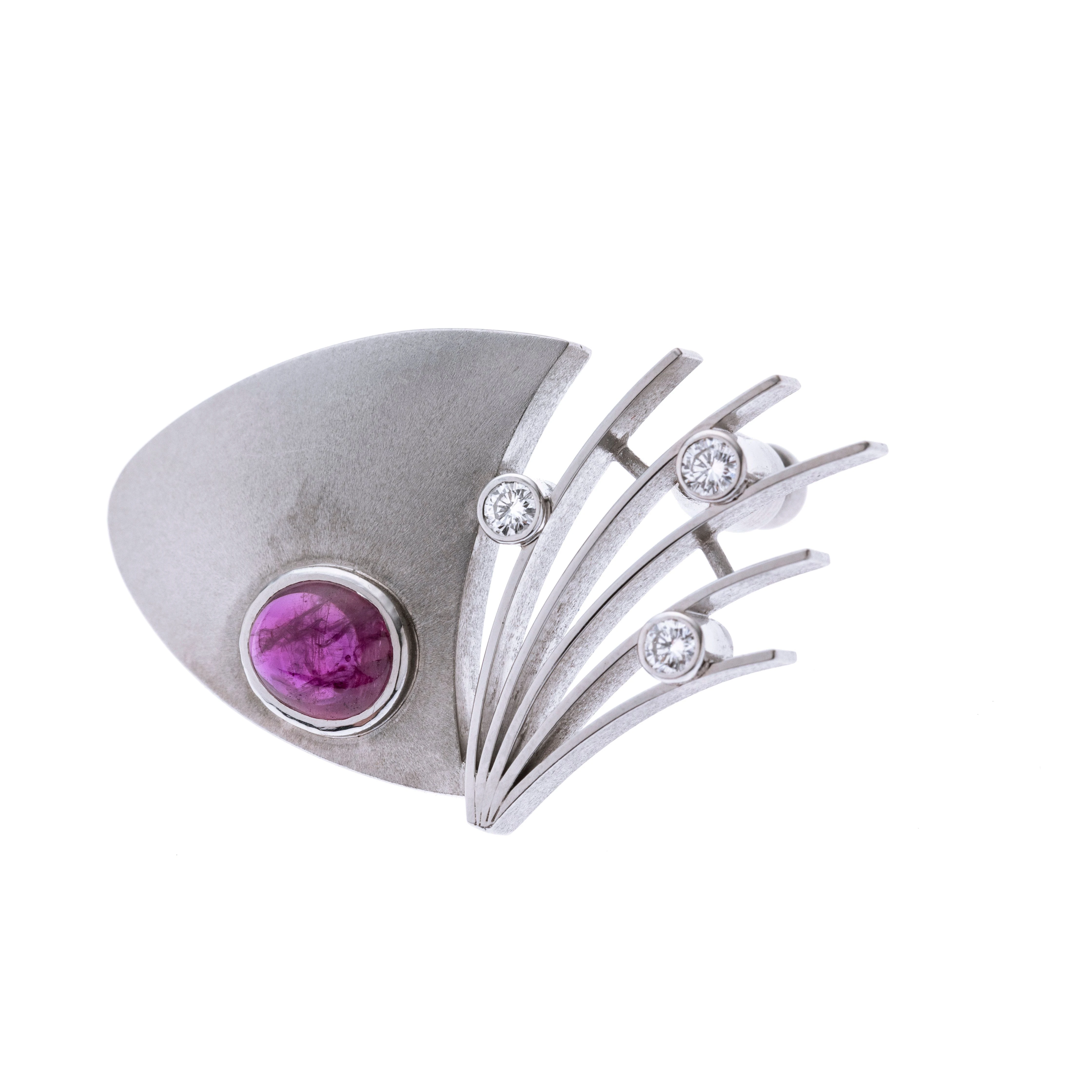 Eine futuristische Brosche aus einem abgerundeten, mattierten, dreieckigen Element mit einem Rubin-Cabochon und vier Weißgold-Stegen, zwischen denen insgesamt drei Brillanten in Zargenfassungen gefasst wurden. Pinartig zu befestigen.