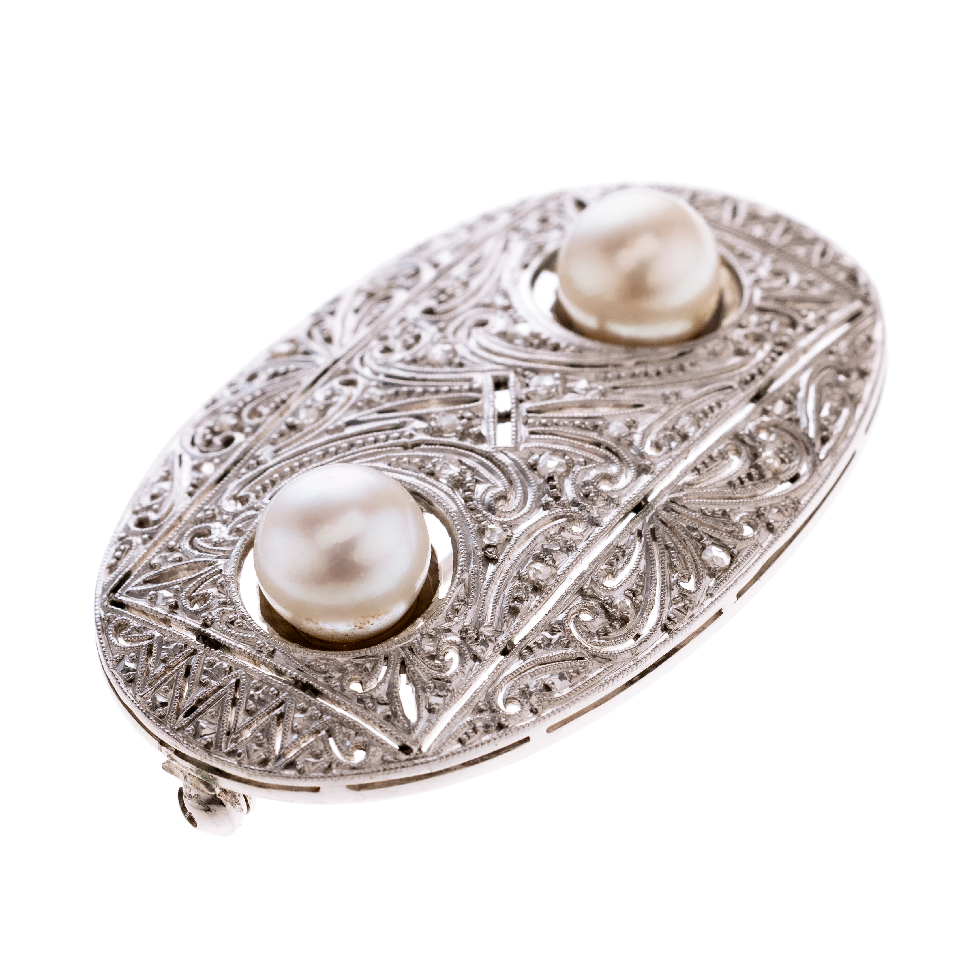 Oval mit floralen ájour gearbeiteten Ornamenten und geometrischen Mustern. von einer Schattenfuge umrahmt werden Zentral zwei Perlen. Die Oberfläche wirkt leicht mattiert und ist Millégriffe verziert und zusätzlich besetzt mit 16 Diamantrosen .