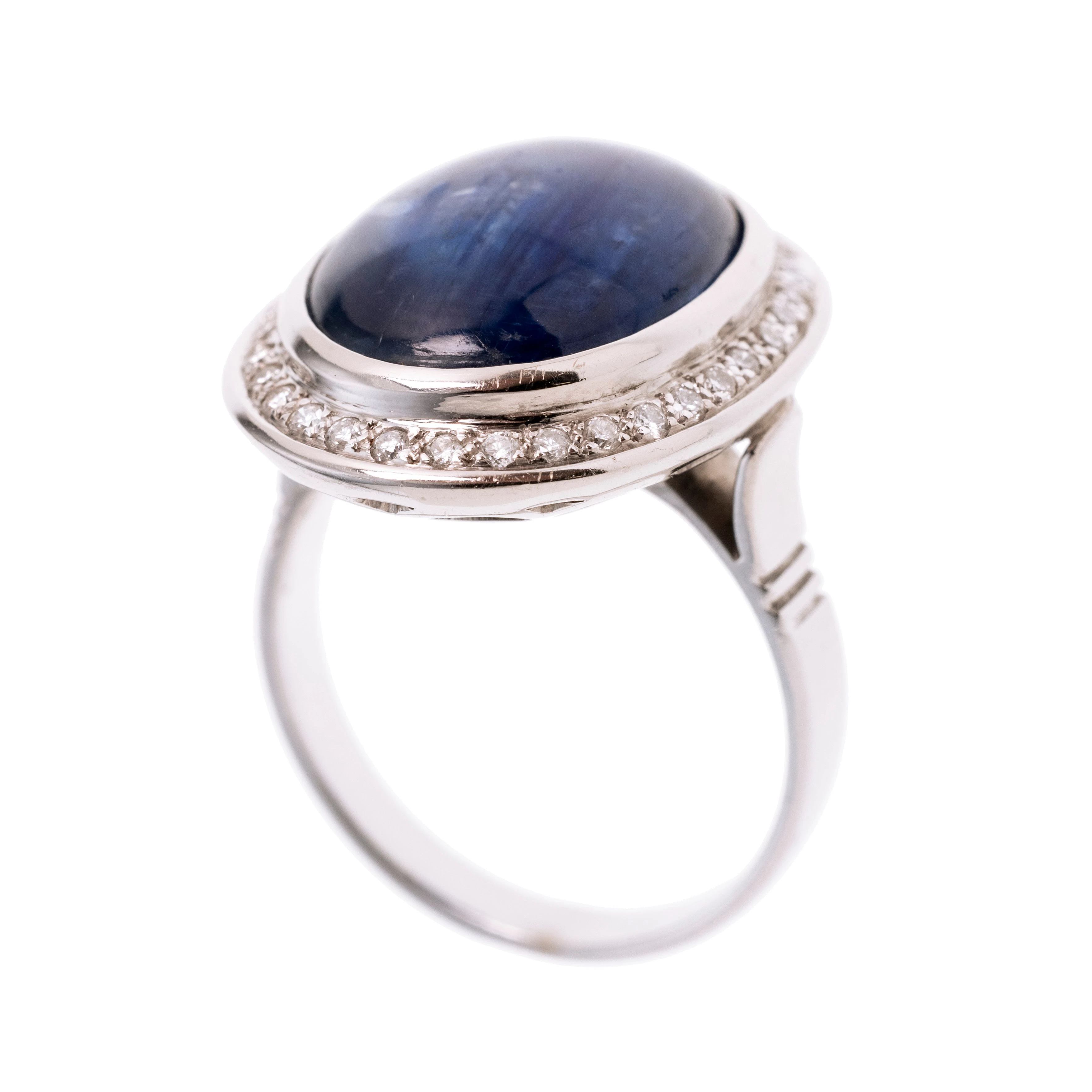 Ein ovaler Saphir-Cabochon (behandelt) in Zargenfassung, der von 34 Brillanten gerahmt wird.