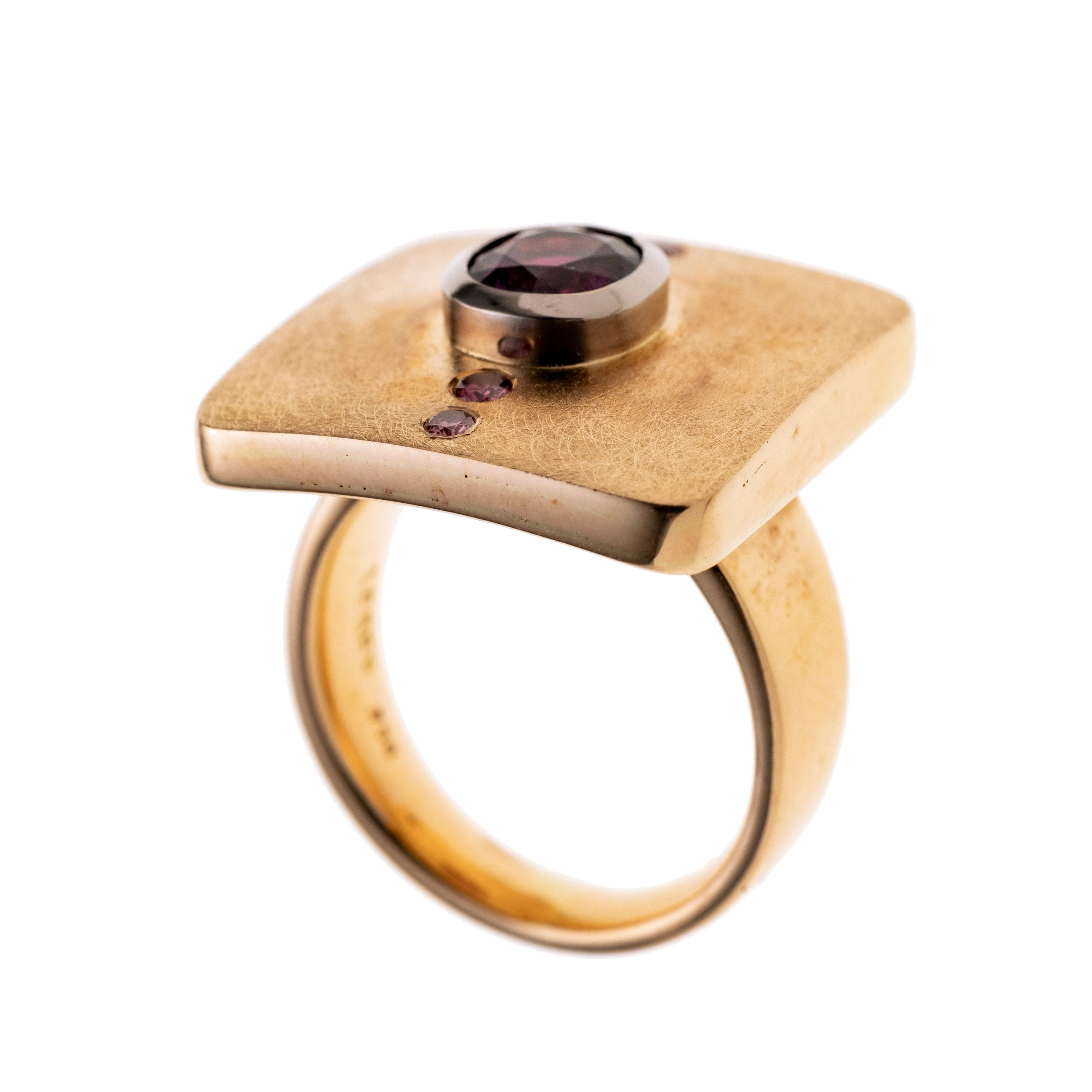Ein Unikat-Ring mit quadratischem Ringkopf, mattiert und insgesamt vier eingeriebenen Magenta farbigen Diamanten (beh.), zusammen ca. 0.136 ct. Mittig leicht erhöht ein ovaler Rhodolith ca. 1.85 ct. weißgoldener Zargenfassung.