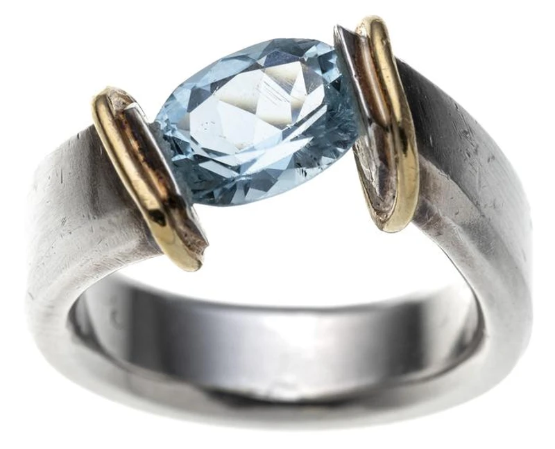 Ein Spannring mit breiter, leicht geschwungener Ringschiene und gelbgoldenen Ringschultern. Mittig befindet sich ein oval geschliffener Aquamarin.