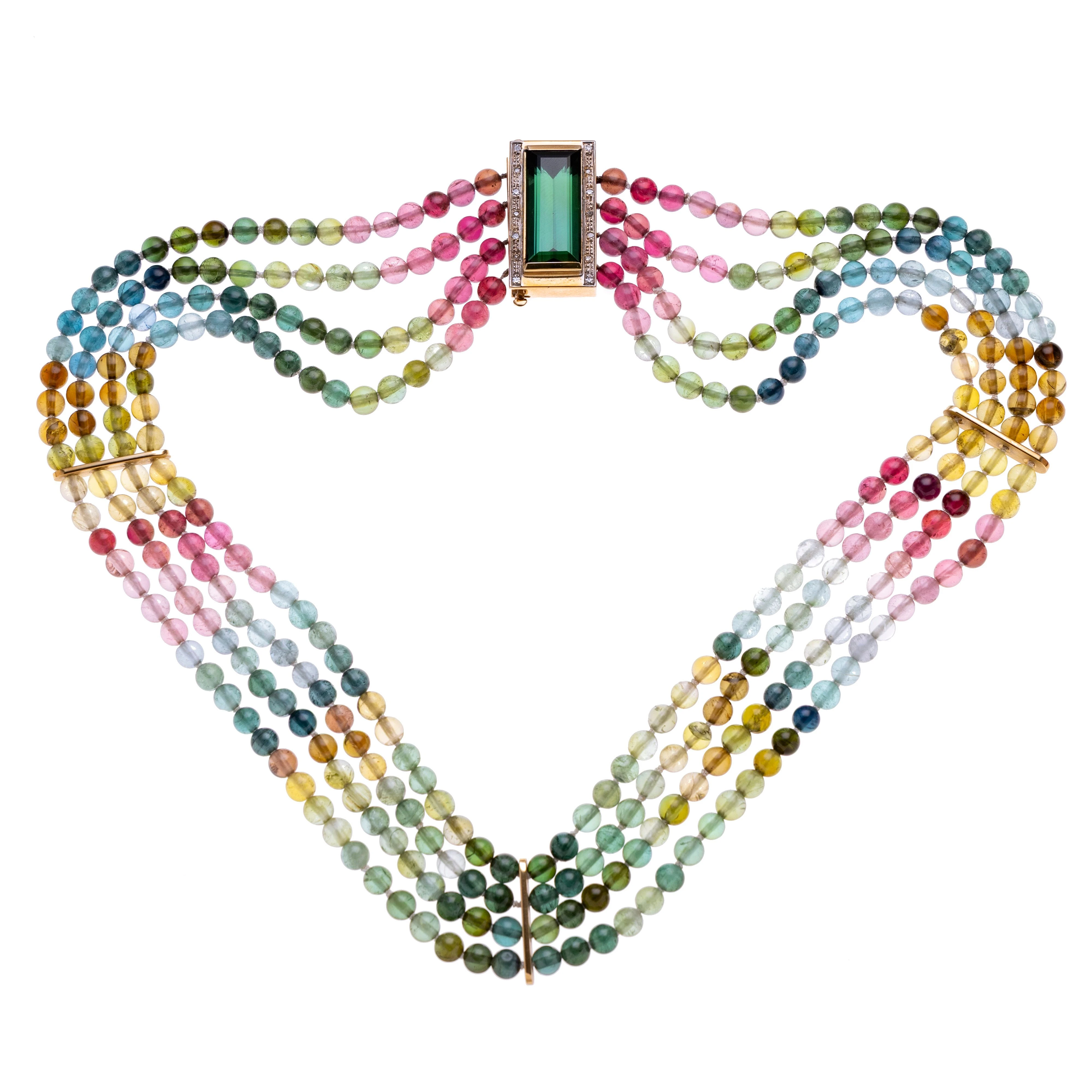 Ein Collier aus vier Strängen bunter Turmalin-Kugeln, die durch drei goldene Kettenschieber unterteilt werden. In der Schliesse befindet sich ein ca. 13,73 ct Turmalin im Smaragdschliff, der von 14 Diamanten je ca. 0.01 ct. flankiert wird.
