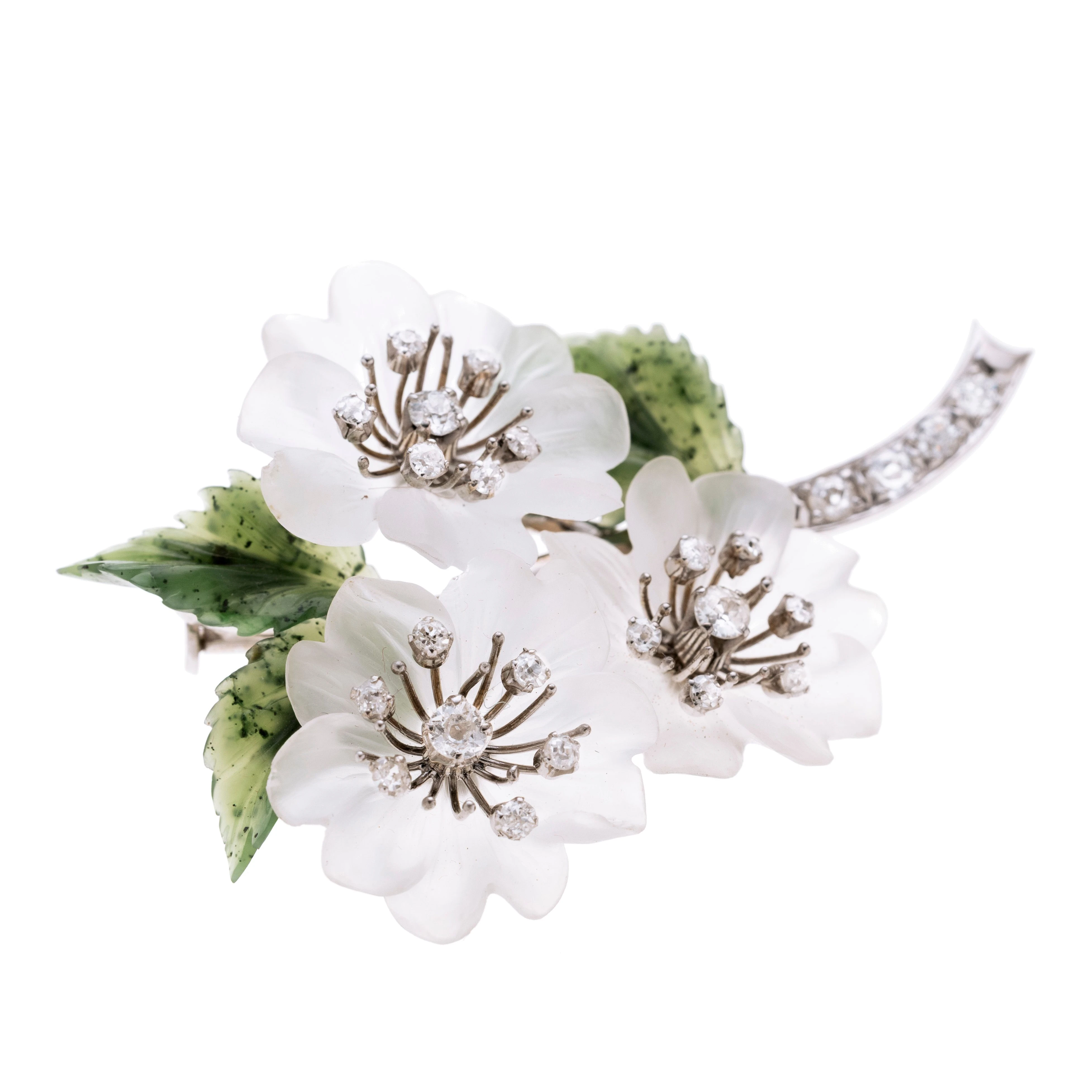 Eine Blumenbrosche aus weißen Blüten, drei mit je sieben Diamanten (zusammen ca. 1,20 ct.) , der Stängel ist mit insgesamt vier Diamanten (insg. ca. 0.40ct) besetzt. Die drei Blätter bestehen aus Nephrit. Signiert